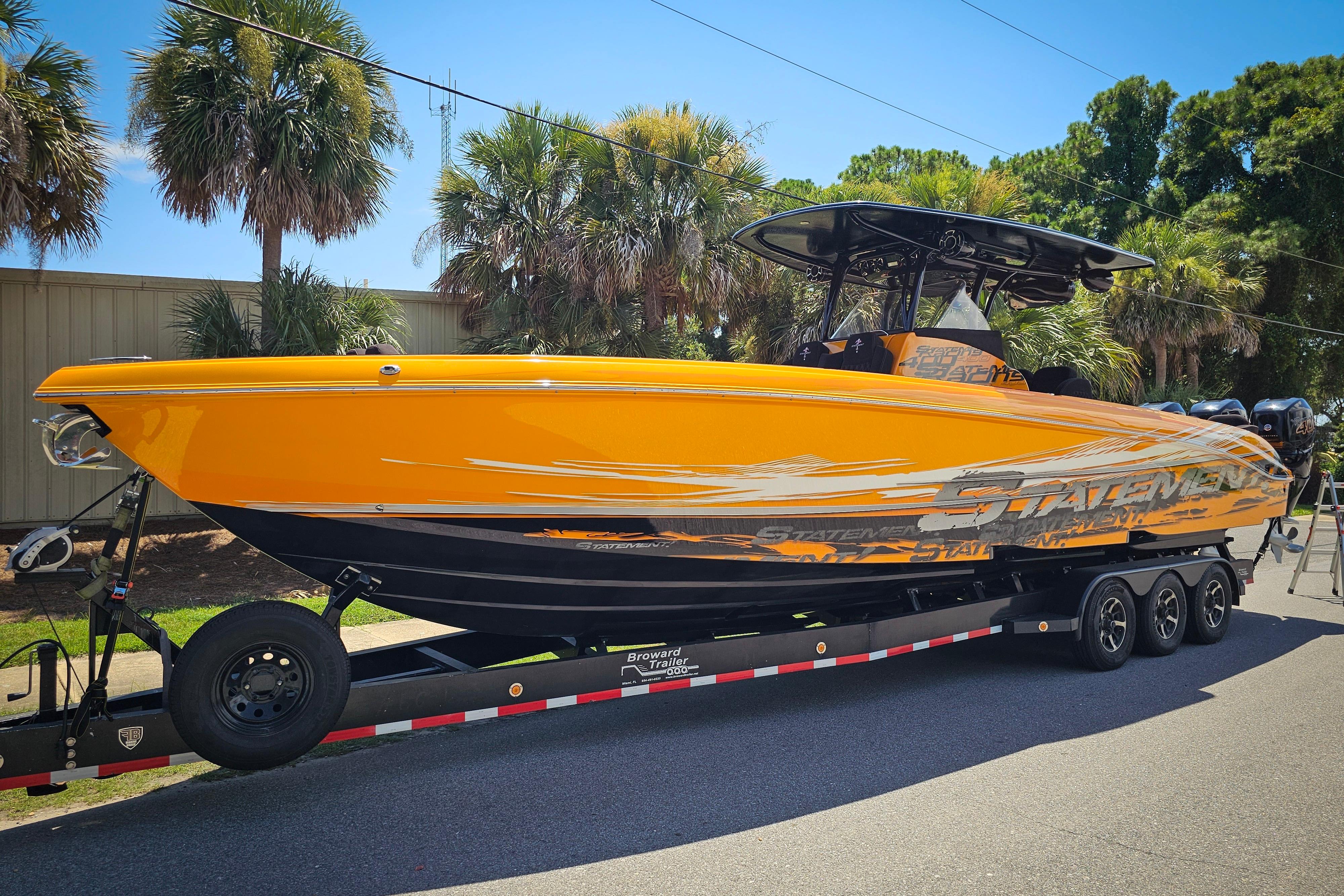 Bright orange 2016 Statement 380 Open boat on trailer, surrounded by palm trees.