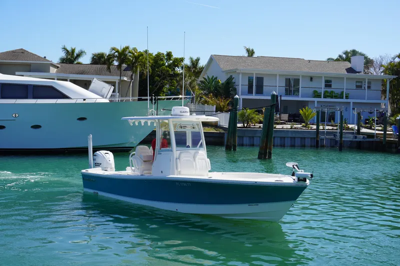  Yacht Photos Pics 2024 Regulator 26XO boat cruising in a sunny waterfront setting with houses and yachts.