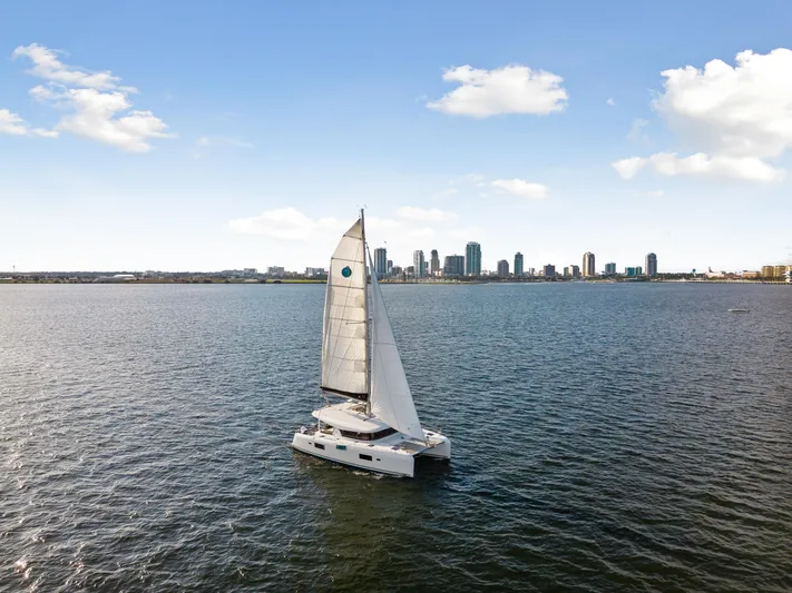 Aquaholic Yacht Photos Pics Lagoon 42 catamaran sailing on open water with city skyline in the background, 2018 model.