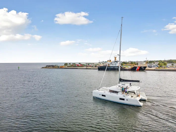 Aquaholic Yacht Photos Pics 2018 Lagoon 42 catamaran sailing near a harbor under a clear blue sky.
