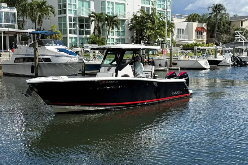  Yacht Photos Pics 2022 Blackfin 272 CC boat cruising in a marina with modern buildings and palm trees.