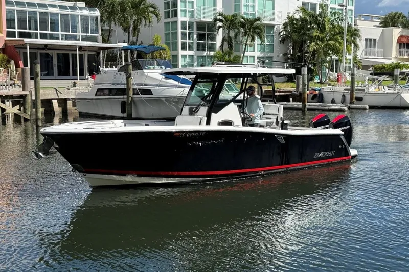  Yacht Photos Pics 2022 Blackfin 272 CC boat cruising in a marina with modern buildings in the background.