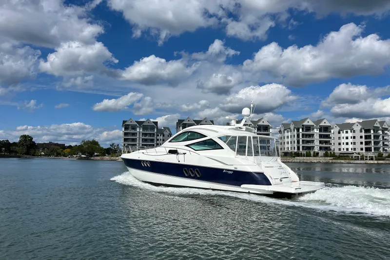 Dolcinea Yacht Photos Pics 2010 Cruisers Yachts 520 Sports Coupe sailing near waterfront buildings under a cloudy sky.