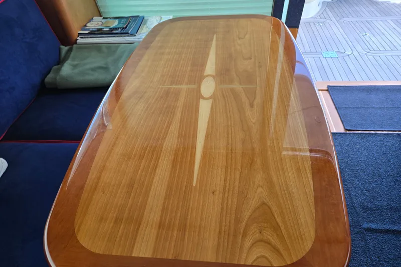 Grayson Yacht Photos Pics Polished wooden table inside 2017 Sabre 48 Fly Bridge yacht, with blue seating and magazines.
