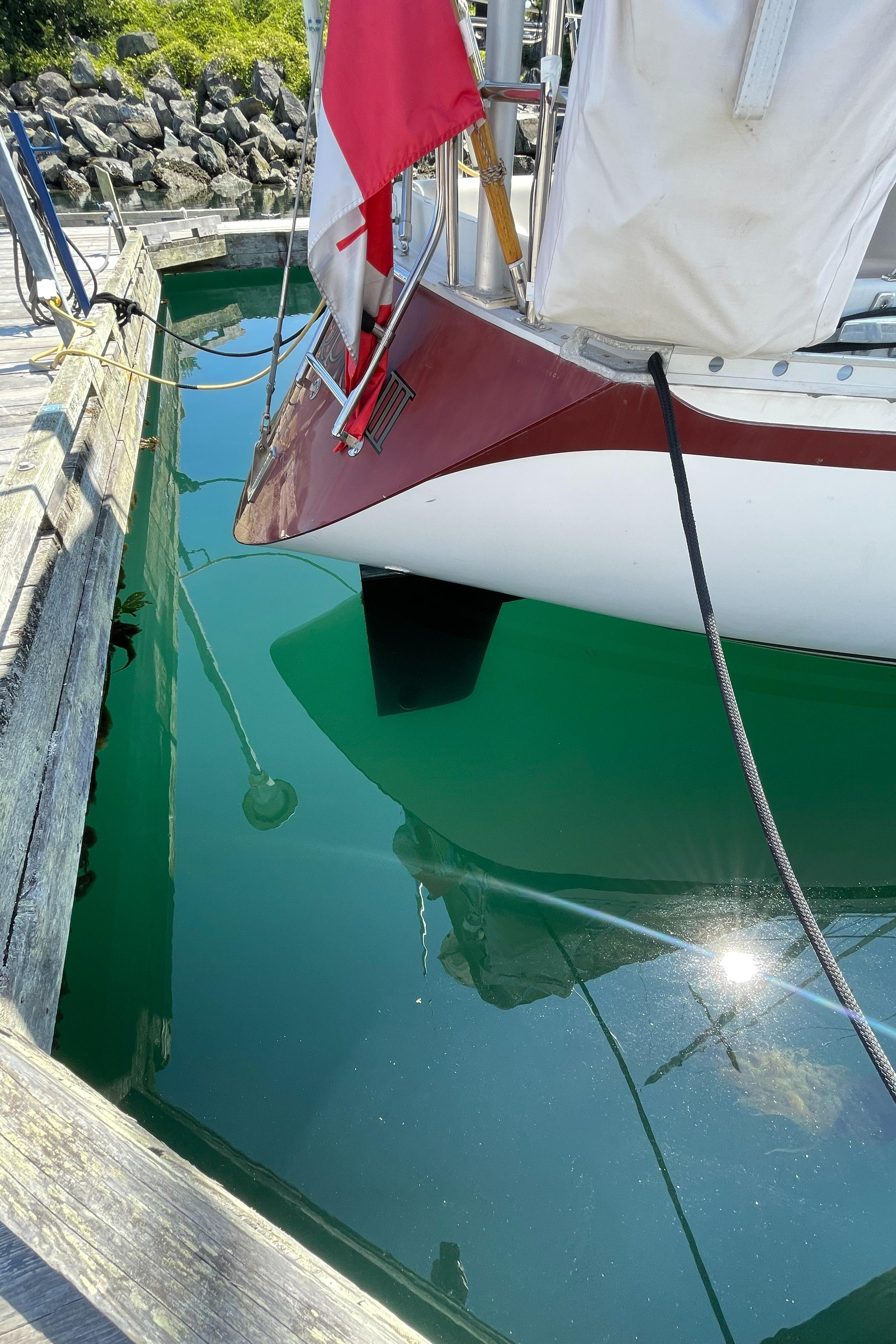 1980 CS 36 Traditional sailboat docked, reflecting in clear water, with a red and white flag.