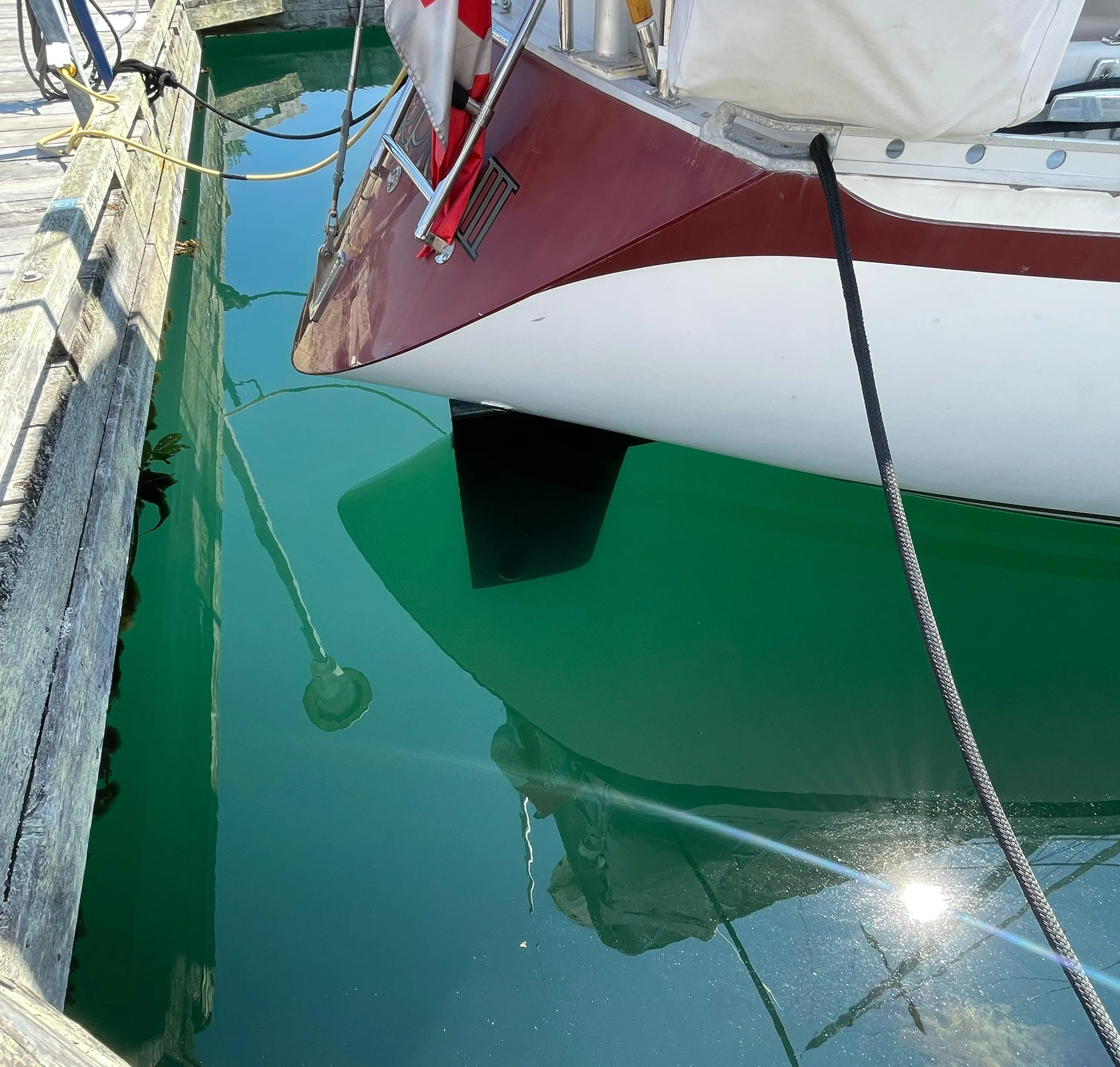 1980 CS 36 Traditional sailboat docked, reflecting in clear water, with a red and white flag.