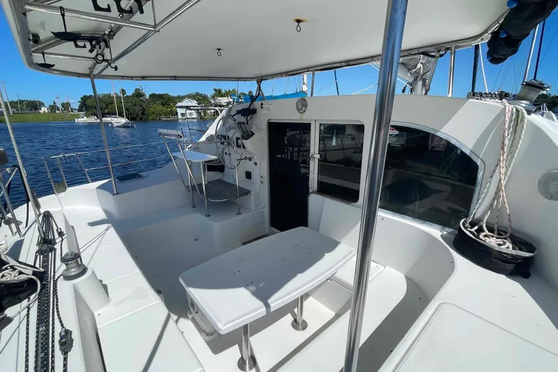 Acushla Yacht Photos Pics 2003 Lagoon 410-S2 catamaran cockpit with seating, table, and helm, docked by the water.