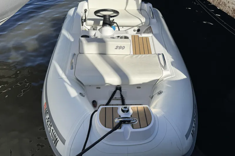  Yacht Photos Pics White inflatable boat docked, featuring wooden accents and steering wheel, near water.