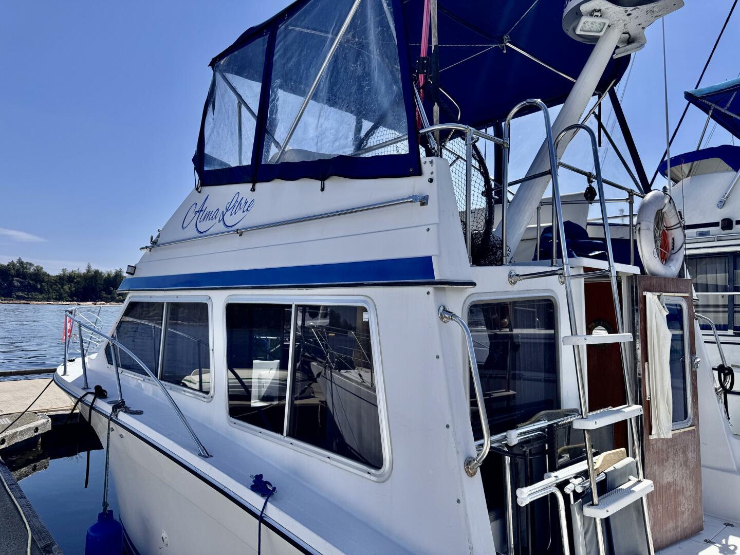 1985 Commander 30 boat docked, featuring blue accents and upper deck canopy.