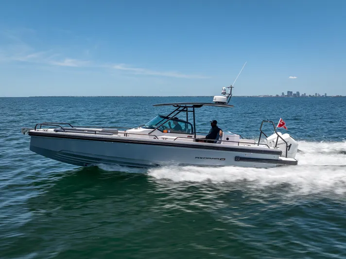  Yacht Photos Pics 2022 Axopar 28 T-Top Brabus cruising on open water, city skyline in background.
