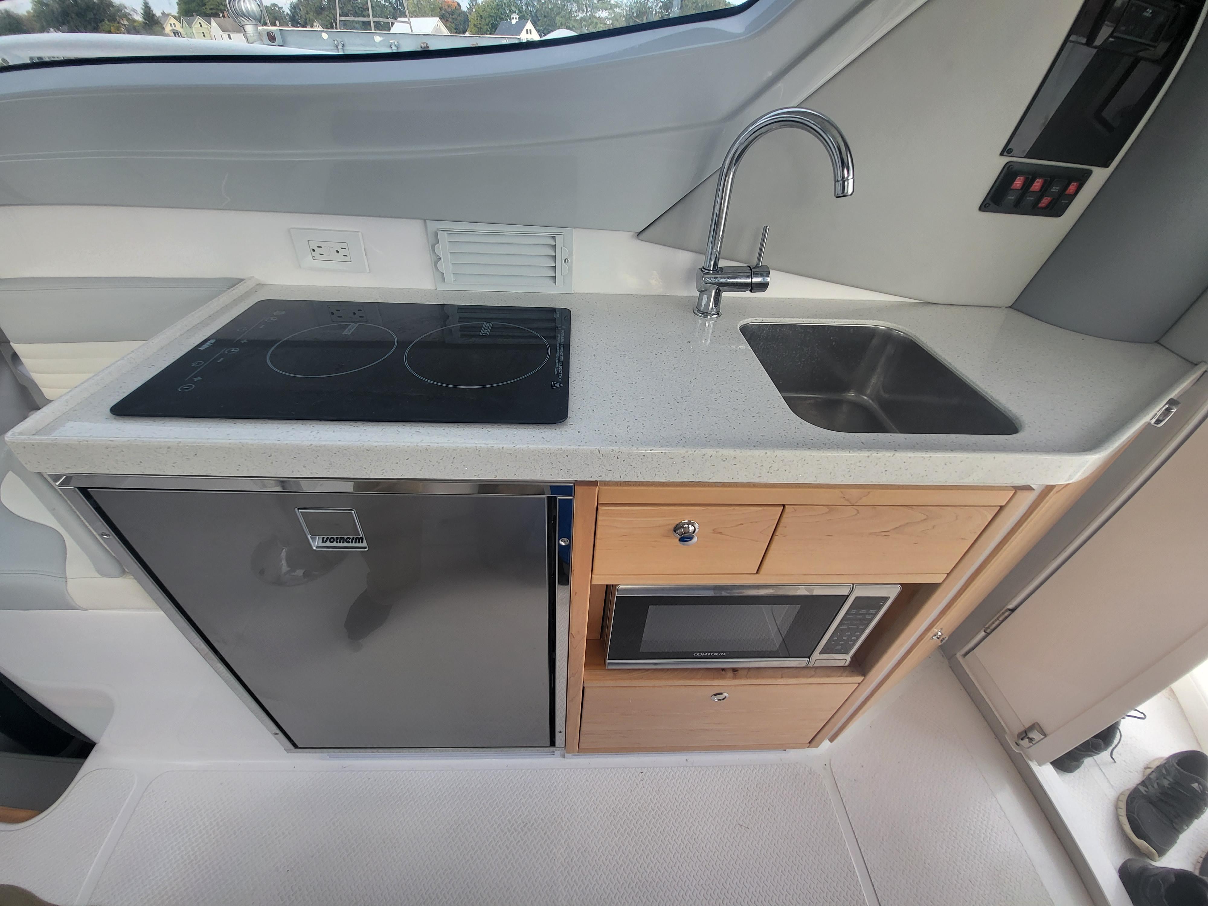 Modern kitchen area in 2024 ArrowCat 320 boat with stove, sink, fridge, and microwave.