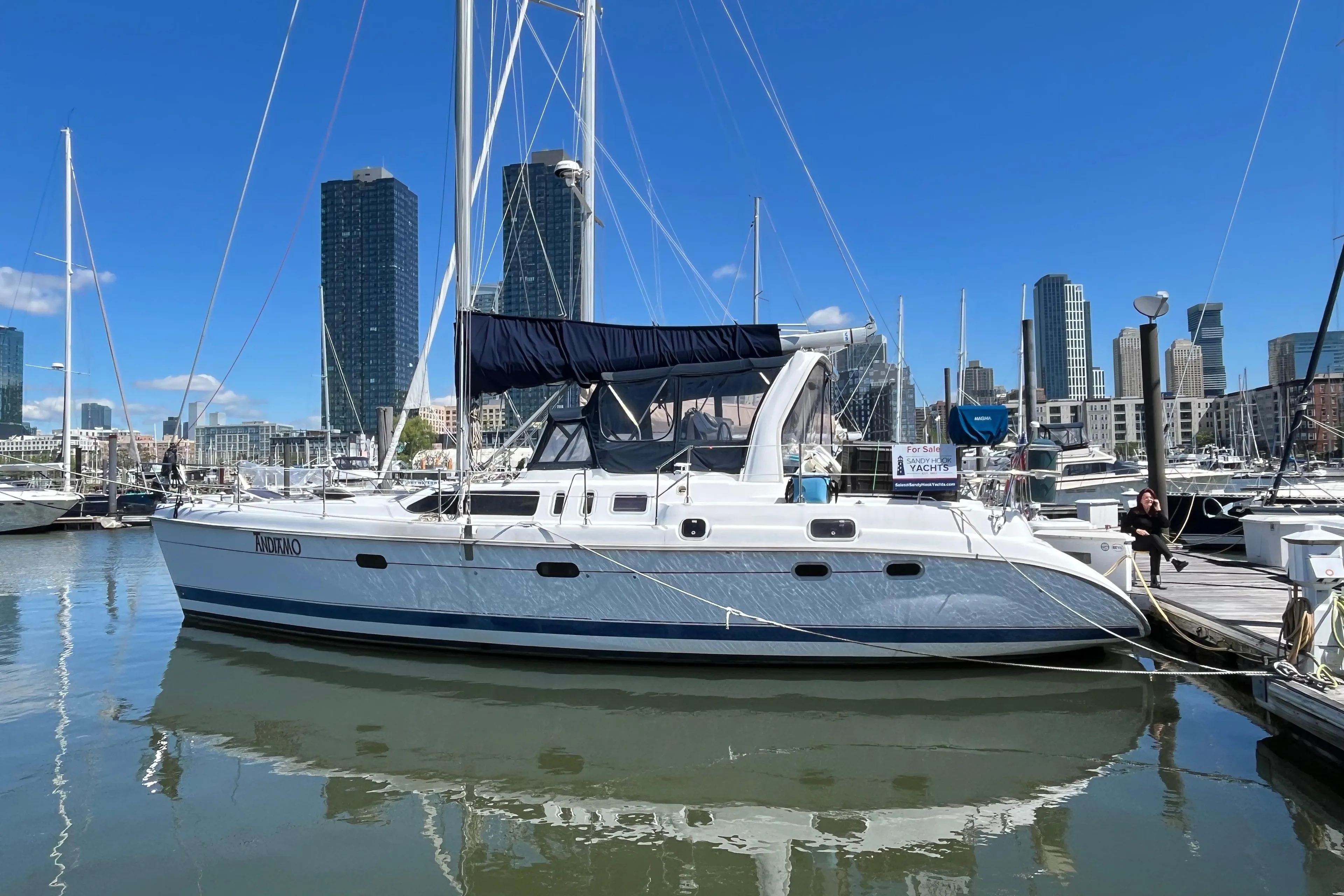 Sailboat docked in marina, 1999 Hunter Passage 450, with city skyline in background.