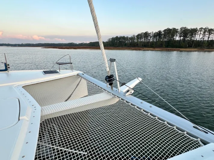 Amihan Yacht Photos Pics 2023 Fountaine Pajot Isla 40 catamaran on calm water near a tree-lined shore.