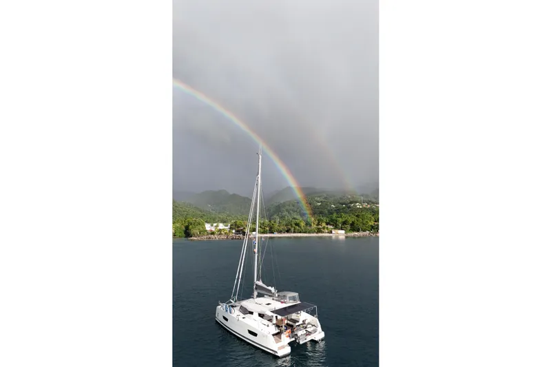 Amihan Yacht Photos Pics 2023 Fountaine Pajot Isla 40 catamaran sailing under a vibrant rainbow near lush coastline.