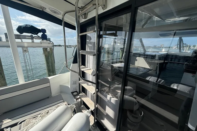 1095-953 Brokerage Josh Yacht Photos Pics 2024 Jeanneau NC Weekender 1095 Fly, interior view with seating and ladder, docked by water.