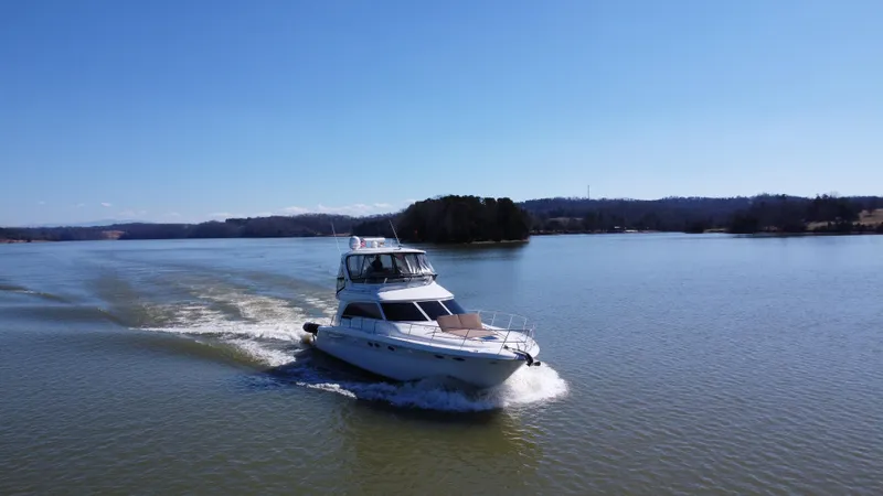  Yacht Photos Pics 2001 Sea Ray 480 Sedan Bridge cruising on a serene lake under clear blue skies.