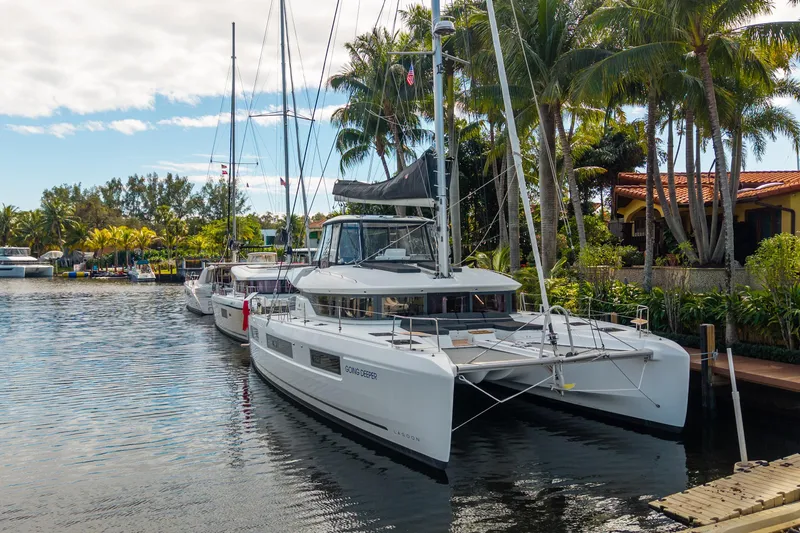 Going Deeper Yacht Photos Pics 2024 Lagoon 51 catamaran docked by tropical waterfront with palm trees.