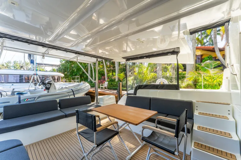 Going Deeper Yacht Photos Pics Luxurious 2024 Lagoon 51 yacht interior with seating and dining area, docked near lush greenery.