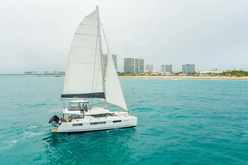 Going Deeper Yacht Photos Pics 2024 Lagoon 51 catamaran sailing near a coastal city skyline.
