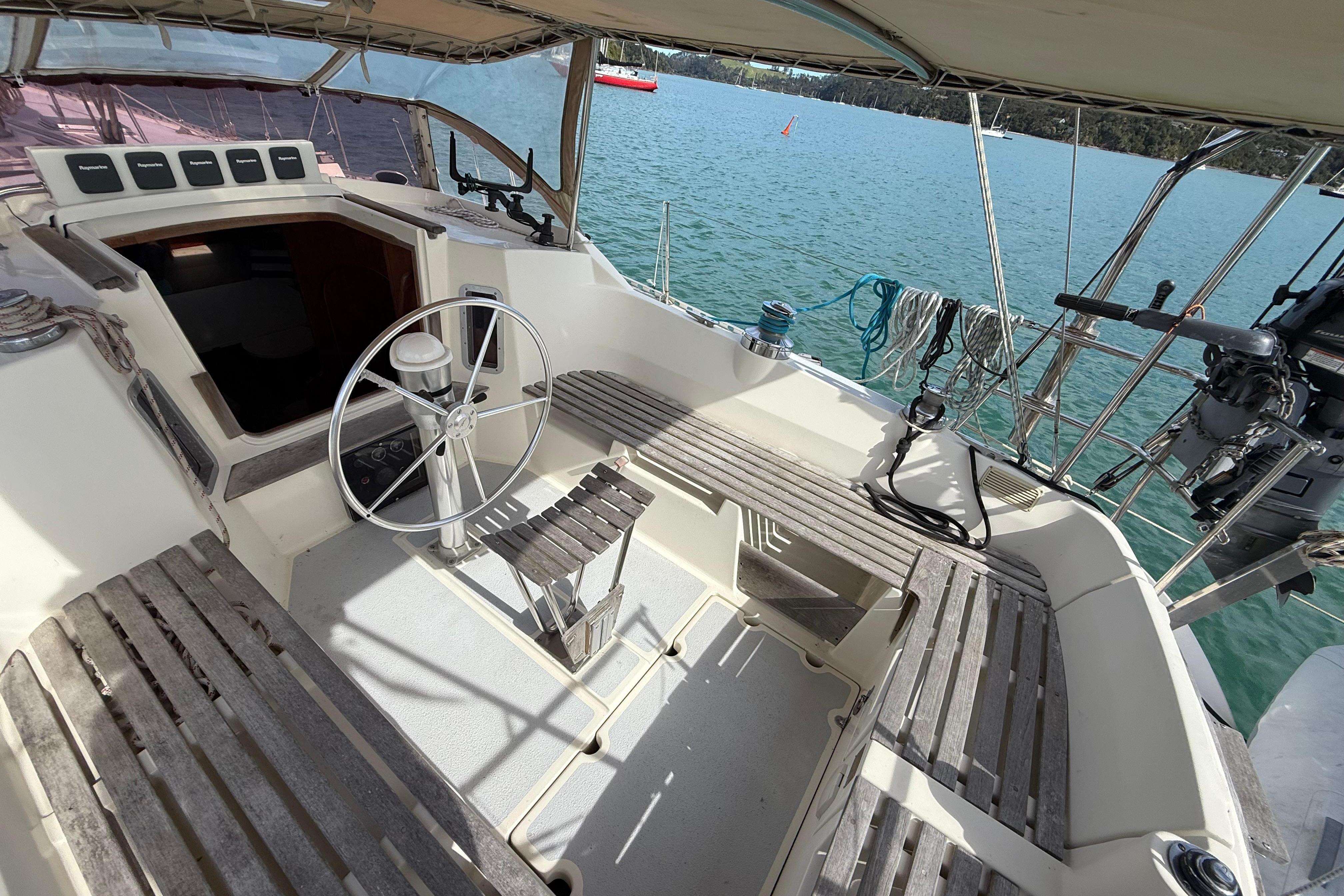 Cockpit of 1983 Express 44 sailboat with wooden seating and steering wheel, docked on calm water.