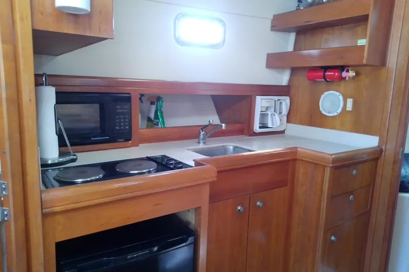 Dolce Far Niente Yacht Photos Pics 2004 Mainship 34 Pilot II galley with stove, microwave, sink, and wooden cabinetry.