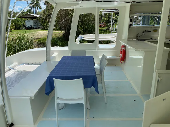 Mirage Yacht Photos Pics Spacious boat interior with table, chairs, and kitchenette, surrounded by lush greenery.
