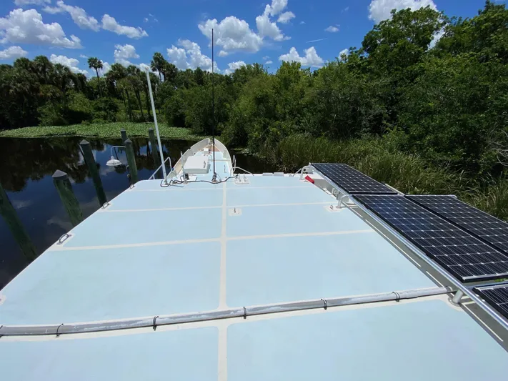 Mirage Yacht Photos Pics Custom 62 boat with solar panels, docked in a lush, green riverside setting, under a blue sky.
