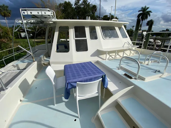 Mirage Yacht Photos Pics Deck of a 1996 Custom 62 boat with table and chairs, under a cloudy sky.