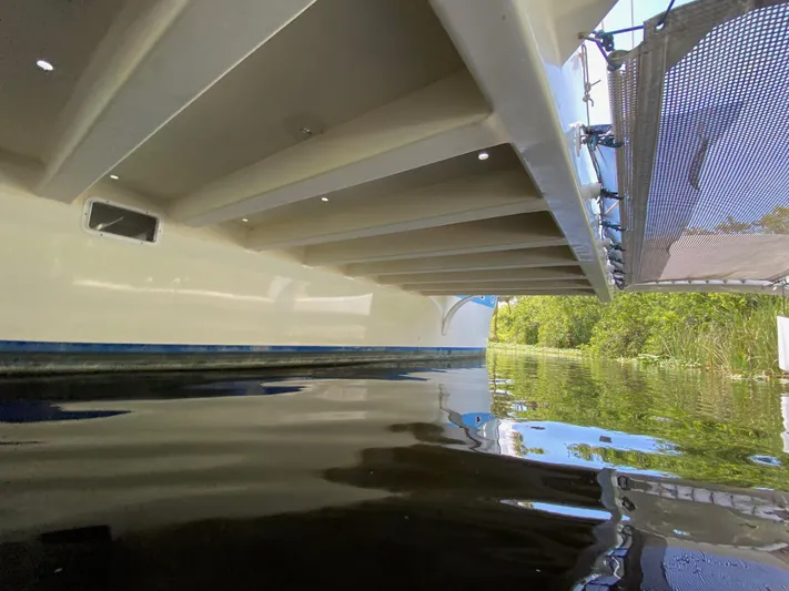 Mirage Yacht Photos Pics Underneath view of a Custom 62 boat on calm water, surrounded by greenery.