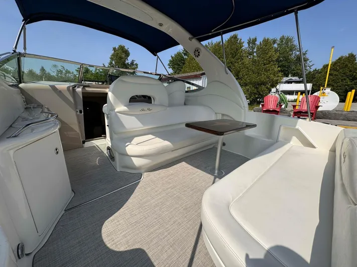  Yacht Photos Pics 2002 Sea Ray 360 Sundancer interior with white seating and a wooden table under a blue canopy.