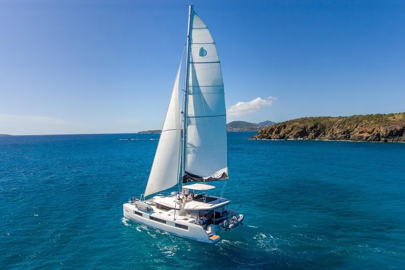 Scuba Doo Yacht Photos Pics 2020 Lagoon 50 catamaran sailing in clear blue ocean near rocky coastline.