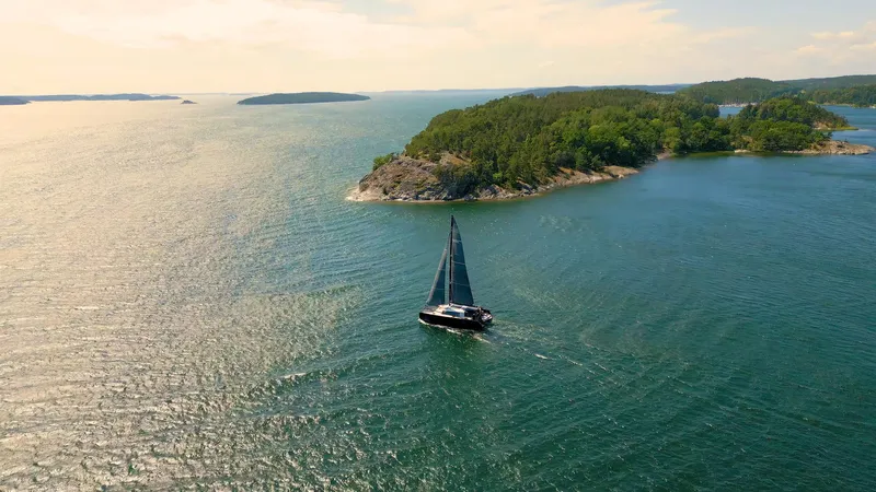  Yacht Photos Pics Sailboat Vaan R5 (2025) navigating serene waters near lush islands.