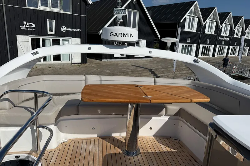 F50199 Yacht Photos Pics 2024 Princess F50 yacht deck with seating and wooden table, docked near modern buildings.