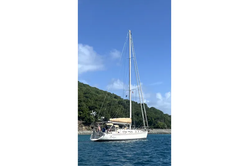 Pratique Yacht Photos Pics Sailboat Outbound 46, 2012 model, anchored near lush green island.