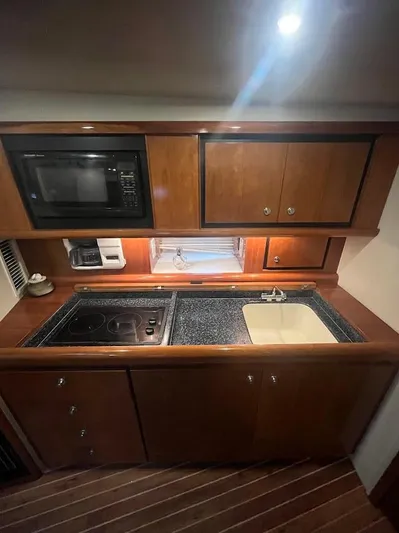 Permanent Waves Yacht Photos Pics 2000 Carver 440 Hardtop Express kitchen with microwave, stove, sink, and wooden cabinets.