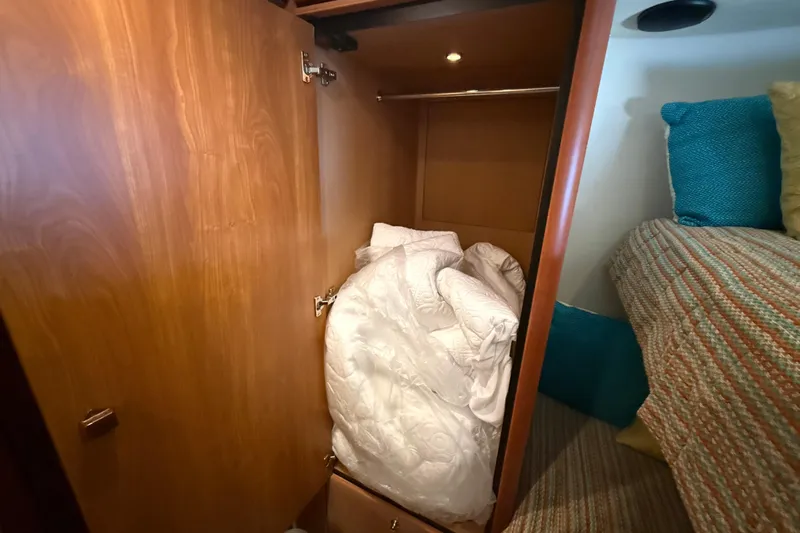 Seaya II Yacht Photos Pics Wooden closet with bedding inside, adjacent to a bed with colorful pillows on a Sunseeker Manhattan 50 yacht.