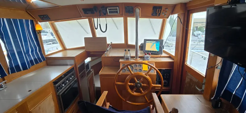 Interlude Yacht Photos Pics 1987 Grand Banks 36 Classic yacht interior with wooden helm, navigation equipment, and blue-striped curtains.