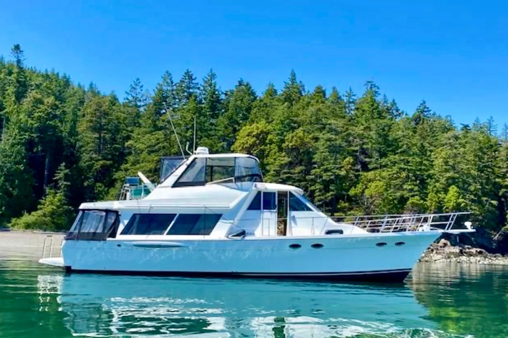 2004 Meridian 490 Pilothouse yacht on serene water with forested background.