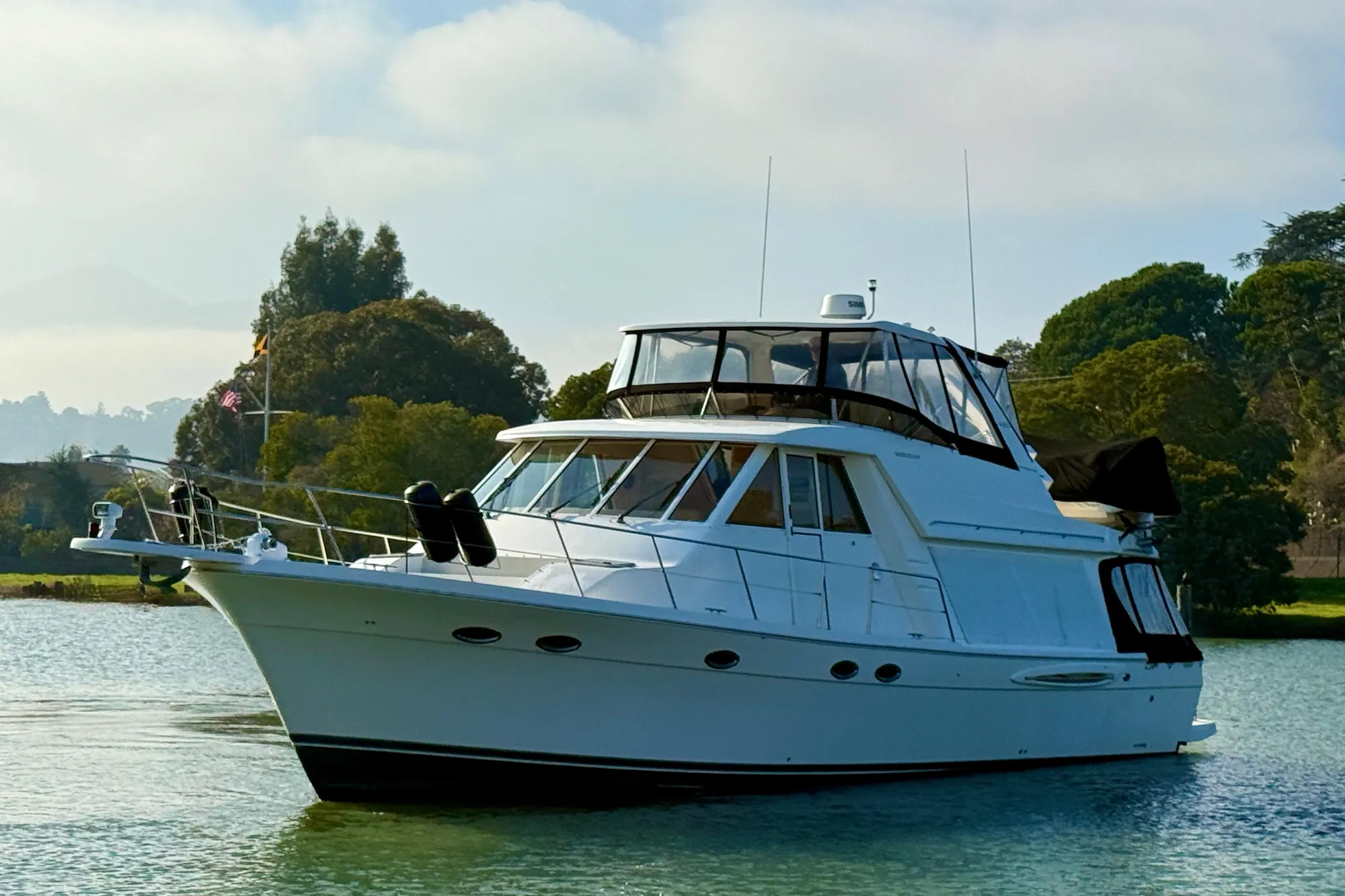 2004 Meridian 490 Pilothouse yacht on calm water, surrounded by lush greenery.