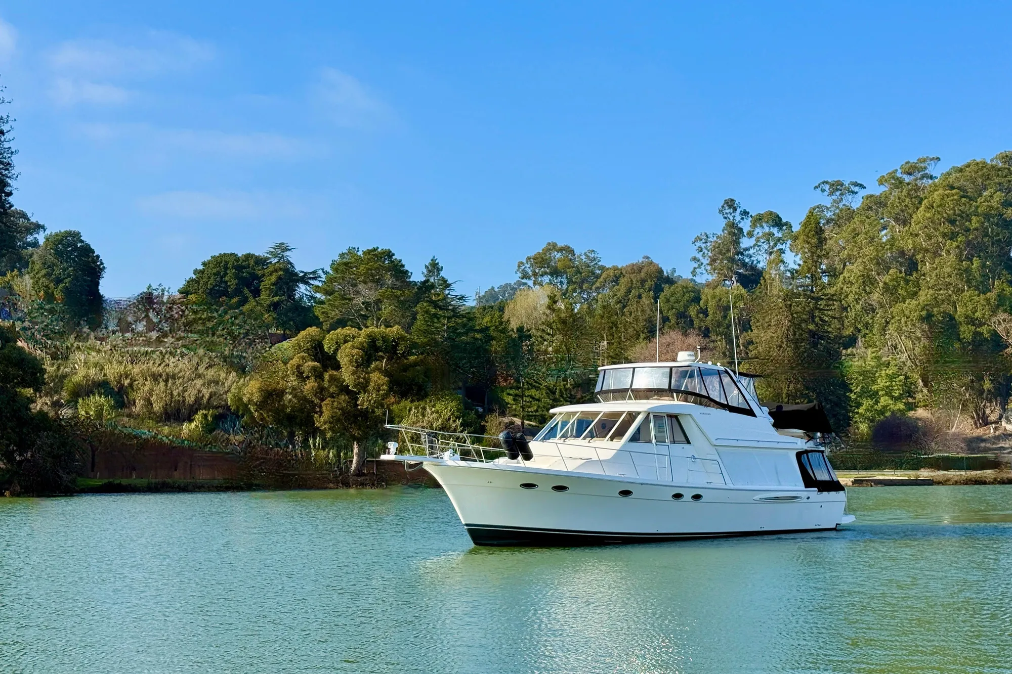 2004 Meridian 490 Pilothouse yacht cruising on a serene lake with lush greenery.