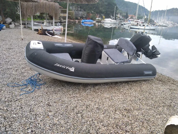  Yacht Photos Pics A black inflatable boat on a pebbled shore near a marina with sailboats.