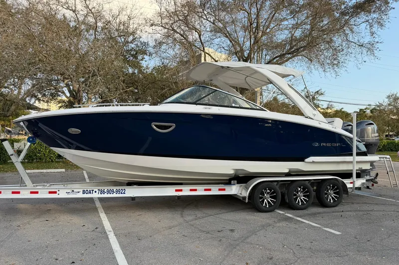  Yacht Photos Pics 2019 Regal 29 OBX boat on trailer, parked outdoors, showcasing sleek design and blue hull.