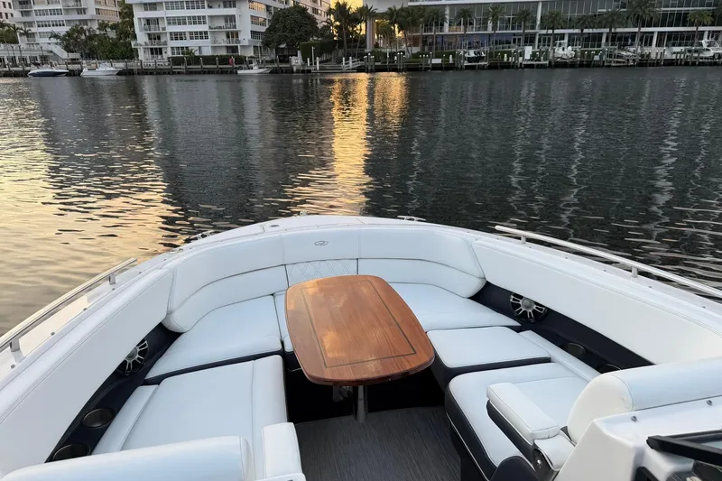  Yacht Photos Pics 2019 Regal 29 OBX boat interior with elegant seating and wooden table, docked by waterfront buildings.