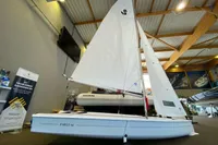 2023 Beneteau First 14 sailboat displayed indoors with white sails.