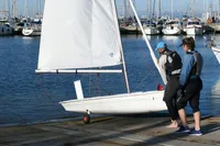 Two people launching a 2023 Beneteau First 14 sailboat at a marina.