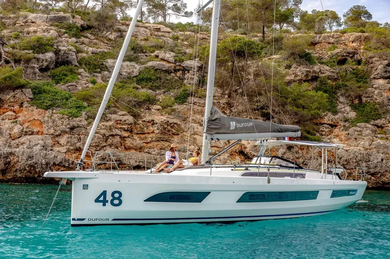  Yacht Photos Pics 2025 Dufour 48 yacht anchored in turquoise waters near rocky coastline.