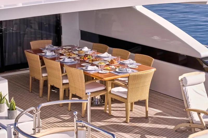 Let It Be Yacht Photos Pics Luxurious dining setup on 1998 Tecnomarine 118 yacht deck, featuring elegant tableware and wicker chairs.