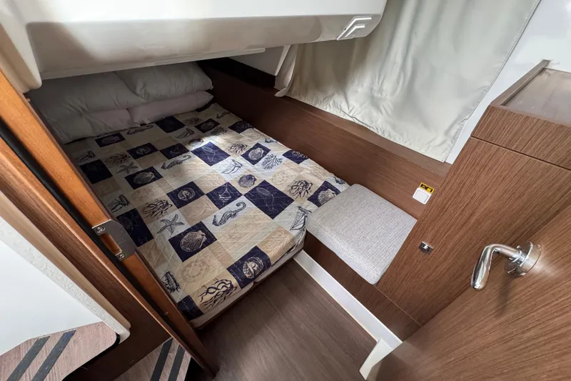  Yacht Photos Pics Cozy cabin interior of 2022 Jeanneau NC Weekender 1095 with nautical-themed bedding.