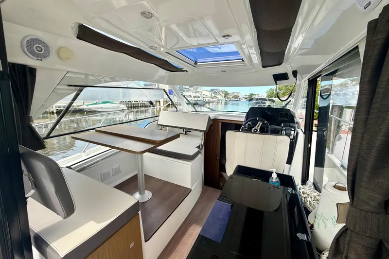  Yacht Photos Pics Interior of 2021 Beneteau Antares 9 boat, featuring seating and helm, docked by the water.