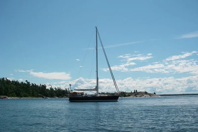 Mistral X Yacht Photos Pics Sailboat Tartan 4300 (2009) on calm water with scenic forested shoreline.